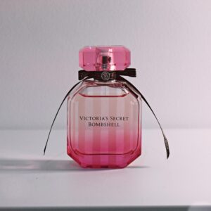 Stylish pink perfume bottle with bow and intricate cap on a white surface.
