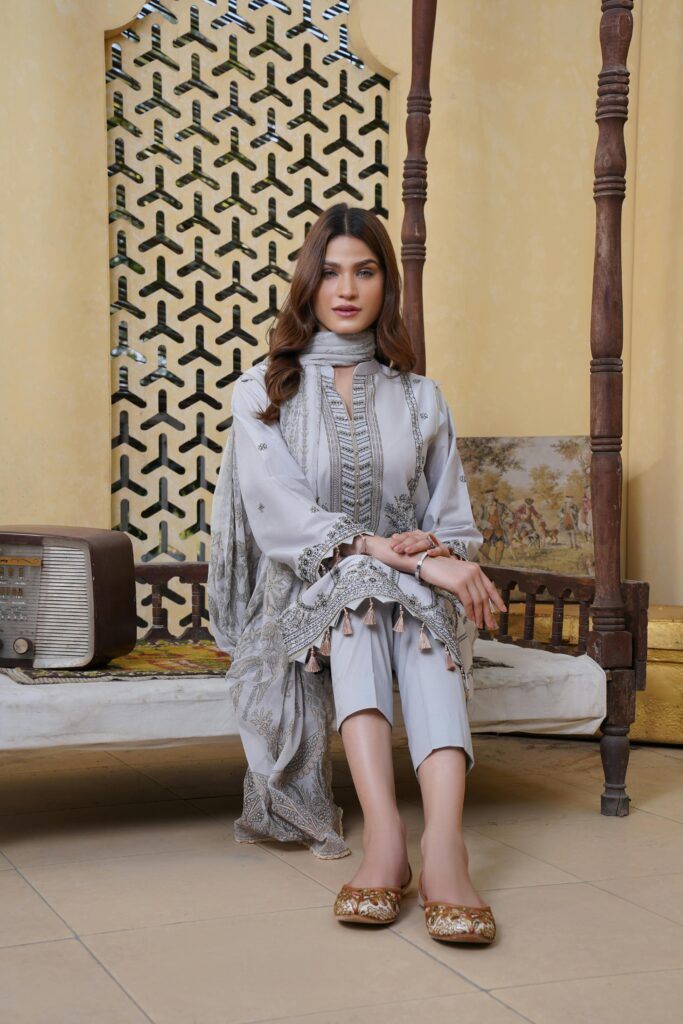 A woman gracefully poses in a stylish, traditional outfit on ornate furniture indoors.
